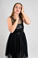 Fototapeta premium Universal concept vertical woman portrait on a white background. A photo of a pretty smiling girl with long hair and excellent make-up in a black dress is standing in various poses in the studio.