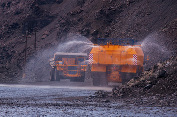 Heavy truck pours the road with water in the iron ore quarry. Dust removal, protection of the...