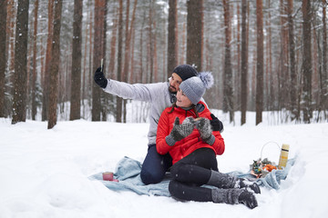 Fototapeta na wymiar young couple have picnic in snowy forest, take selfie