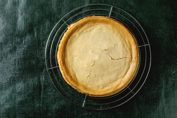 Whole homemade cane sugar baked cheesecake on cooling rack over dark texture background. Flat lay, space