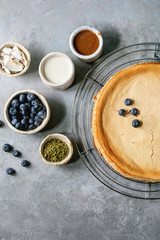 Homemade cane sugar baked cheesecake on cooling rack with variety of toppings in ceramic bowls over grey texture background. Flat lay, space