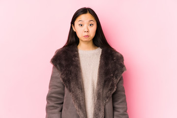 Young chinese woman wearing a coat isolated shrugs shoulders and open eyes confused.
