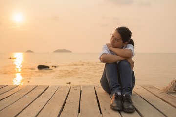 Woman sitting alone With anxiety And disappointed in the stories In the setting sun At the wooden bridge in the ocean
