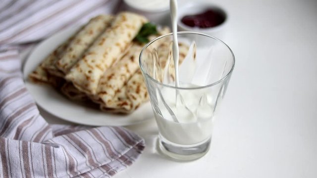 Breakfast with pancakes and milk. Milk is poured into a transparent glass. In the background is a plate and a fresh napkin. Copy space.