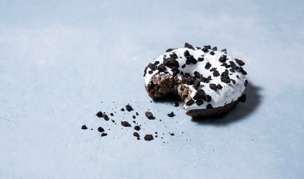 one delicious fresh hearty black and white bitten donut lie on a blue background. jank food and high-calorie food