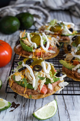 Chicken tostadas with refried pinto beans, fresh cilantro, shredded cheddar cheese, avocados, black olives, sour cream, lettuce, jalapenos, lime and tomatoes. Selective focus with blurred background.