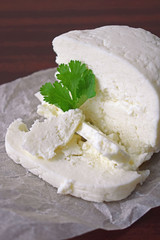 Homemade cheese with a sprig of greenery on a wooden background.