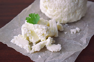 Homemade cheese with a sprig of greenery on a wooden background.