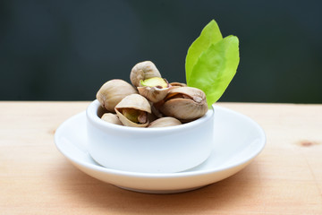  Pistachios on the white wooden background, accompanied by green leaf