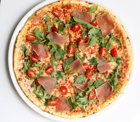 Italian cuisine. Pizza with ham, arugula and tomatoes on a white background. Top view