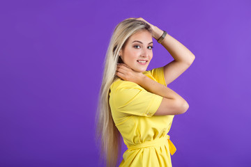 Obraz premium beautiful young woman in a yellow dress on a purple background with her hair