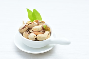  Pistachios on the white wooden background, accompanied by green leaf