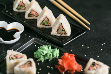 Japanese surimi quinoa rolls with pickled ginger and wasabi sauce on a black plate with chopsticks on a dark background.