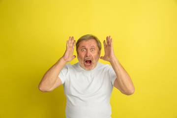 Astonished, shocked, wondered. Caucasian man portrait isolated on yellow studio background. Beautiful male model in white shirt posing. Concept of human emotions, facial expression, sales, ad.
