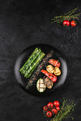 Grilled vegetables on a black plate. Asparagus, bell pepper, zucchini, eggplant, potatoes and tomatoes baked on the fire.