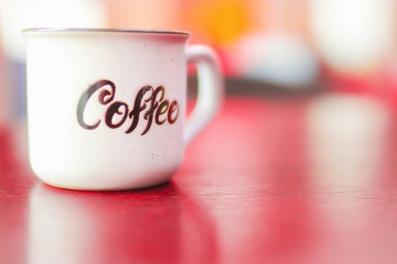 Enamel white metal mug with  inscription  coffee on  wooden table on blurred background. Place for text or advertising
