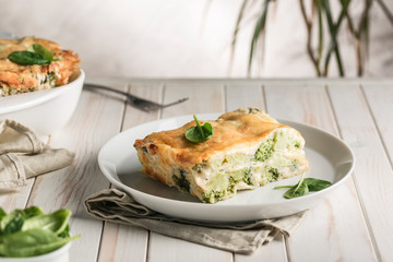 Italian lasagna with spinach and broccoli on white plate on bright background with copyspace.
