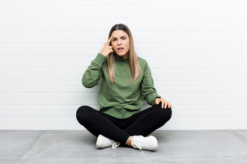 Fototapeta na wymiar Young caucasian woman sitting on the floor showing a disappointment gesture with forefinger.