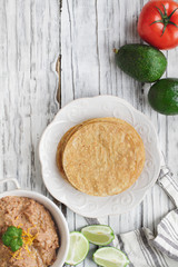 Corn tortillas with refried beans, avocados, tomatoes and fresh limes to make vegan tostadas. Photo shot from top view.