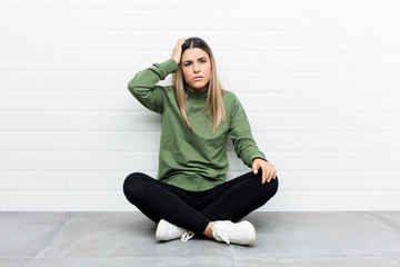 Young caucasian woman sitting on the floor tired and very sleepy keeping hand on head.