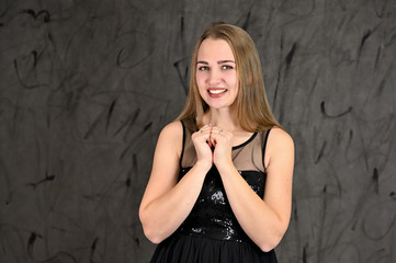 Naklejka premium Universal concept of horizontal female portrait on gray alternative background. A photo of a pretty smiling girl with long hair and excellent make-up in a black dress stands in different poses.