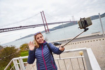 Young woman tourist take selfies on the background of famous iron 25th of April bridge in Lisbon city, Portugal