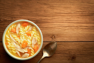 Top view of a bowl of chicken noodle soup and spoon on a wooden rustic background with copy space