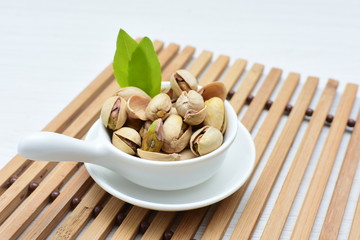  Pistachios on the white wooden background, accompanied by green leaf