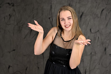 A photo of a pretty smiling girl with long hair and excellent make-up in a black dress stands in different poses. Universal concept of horizontal female portrait on gray alternative background.