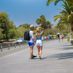 Young beautiful European couple walking along the palm road. They are enjoying their honeymoon.