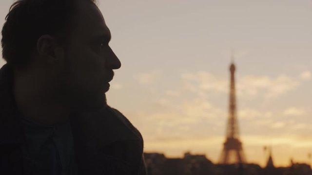 Close-up sunset portrait of thoughtful European young man looking right at Paris Eiffel Tower sky scenery slow motion.