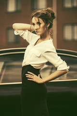 Young fashion business woman in white shirt and pencil skirt next to her car