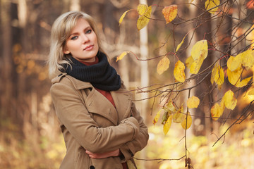 Happy young fashion woman in beige coat walking in autumn park