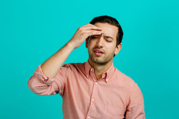 Portrait of a young adult man with a headache,  isolated on blue studio background