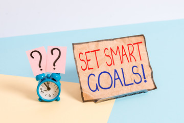Writing note showing Set Smart Goals. Business concept for list to clarify your ideas focus efforts use time wisely Alarm clock beside a Paper sheet placed on pastel backdrop