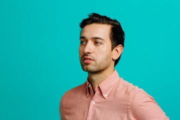 Portrait of a young adult man looking to side thinking,  isolated on blue studio background