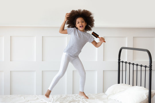 Girl jumping on bed holding hairbrush like microphone and singing