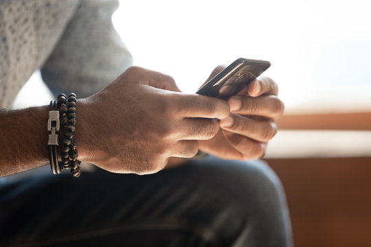Close up african guy sitting indoors holding in hands smartphone