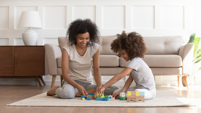 African mother and daughter playing with toy blocks set indoors