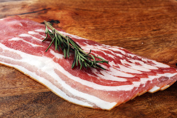 Fresh cold sliced bacon with rosemary on the wood background. Delicious bacon