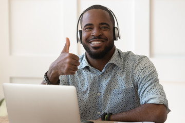 African guy in headphones sitting near computer showing thumbs up