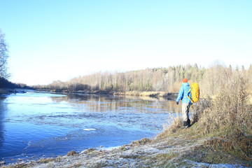 Fototapeta premium traveler with a backpack by the river / tourist guy on a northern hike, winter trip