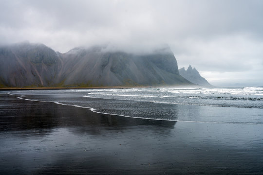 Waves are crashing ashore on Stokksnes peninsula black beach with vestrahorn mountain chain in the background. Travel and landscapes in Iceland concept.