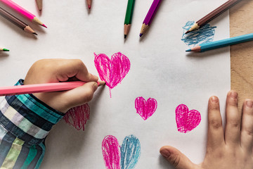 Baby hand with pencil heart drawing. Concept for Valentines Day or Mother's Day or Father's Day. A child draws a heart with pencil/pen. Top View.