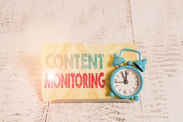 Word writing text Content Monitoring. Business photo showcasing a tool to identify mentions of their organization Mini blue alarm clock stand tilted above buffer wire in front of notepaper