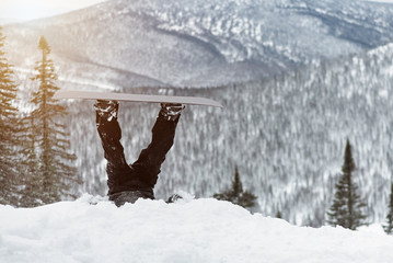 Snowboarder feet sticking out of the snow on a snowy mountains background.