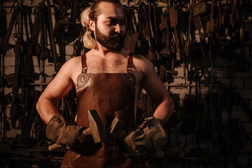 Fototapeta na wymiar Brutal artisan blacksmith standing in a workshop with two hammers close up