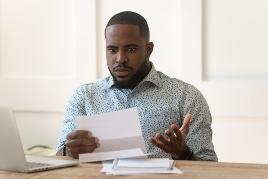 Confused african man holding mail letter reading shocking unexpected news