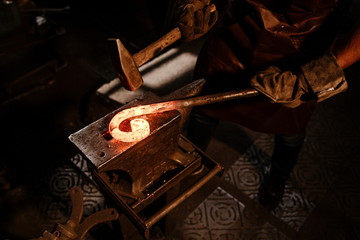 Brutal bearded man in an apron, knocking on red hot metal on an anvil with a hammer