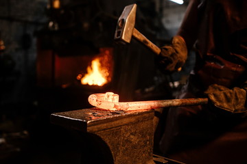 Brutal bearded man in an apron, knocking on hot metal with a hammer close-up